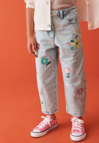 Vaqueros de mezclilla azul claro con bordado floral en varios colores, detalles desgastados y corte recto, combinados con zapatillas rosas.