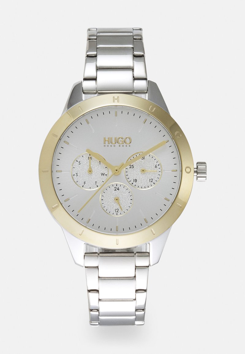 Reloj de pulsera de plata y oro con una esfera redonda, un dial plateado, tres subesferas y una pulsera de metal. Características: superficies pulidas y textura ligera.