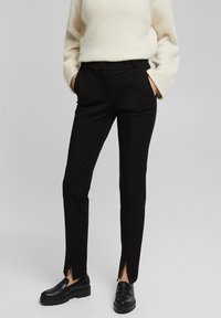 Svarta figurnära byxor med framfickor, med en mjuk textur och skräddarsydd design. Bärs med svarta loafers och en elfenbensfärgad tröja.