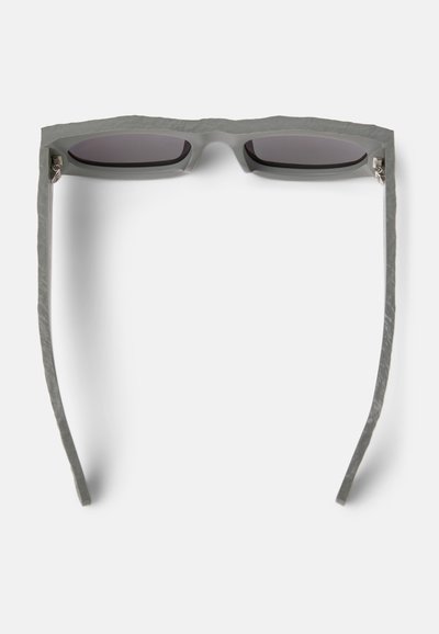 Grijze zonnebril met een gestructureerd, hoekig montuur. Slanke veren en donkere lenzen. Opvallende hardware omvat zilveren accenten bij de scharnieren.