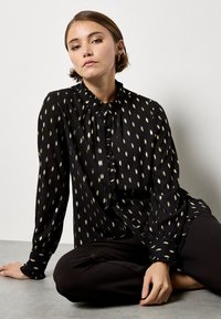 Black blouse with gold leaf patterns, ruffled collar and button front closure. Long sleeves with fitted cuffs. Soft, lightweight fabric.