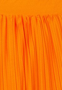 Veckat tyg i klar orange, med en texturerad yta och vertikala linjer som skapar djup och rörelse.