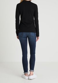 Czarna koszula z długim rękawem, dopasowany krój, w parze z ciemnoniebieskimi dżinsami. Dżinsy podwinięte przy mankietach, białe trampki z metalicznymi akcentami.