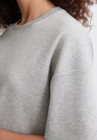 Jasnoszara bluza z krótkim rękawem i okrągłym dekoltem, wykonana z miękkiego materiału. Charakteryzuje się luźnym krojem i subtelną fakturą.