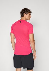Camiseta deportiva rosa de manga corta, con una superficie texturizada y costuras planas. Combinada con pantalones cortos negros, que muestran un diseño ajustado.