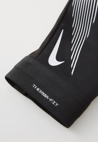 Svart Therma-Fit erme med en teksturert overflate og en hvit Nike-logo med parallelle hvite linjer for ekstra designdetaljer.