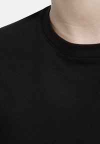 Svart bomullströja med rund hals. Texturen är mjuk och tyget verkar andas, med fin ribbning nära halsringningen.