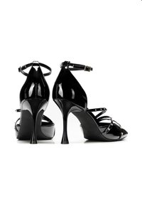 Sandali con tacco alto in vernice nera, dotati di cinturini alla caviglia e caratterizzati da molteplici cinturini sottili e dettagli con borchie. Design elegante con tacco a stiletto.