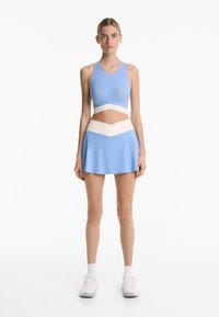 Light blue sports bra with a wide band, paired with a matching skirt featuring a white zigzag pattern at the waist. Soft texture.