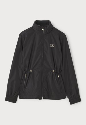 Giacca leggera nera con colletto alto, polsini elasticizzati, vita con cordino e due tasche con zip. Presenta un logo dorato sul petto.