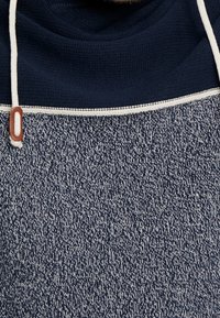 Granatowa bluza z kapturem z teksturowanym dzianinowym korpusem, z białym kontrastowym sznurkiem i ozdobnym przeszyciem. Miękka tkanina o przytulnym wyglądzie.