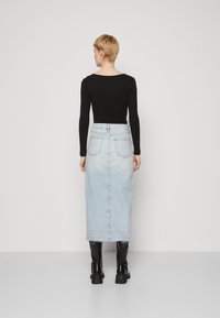Fekete, hosszú ujjú felső, világoskék denim midi szoknyával párosítva. A szoknyán rojtos szegély és két hátsó zseb található. Fekete bokacsizma tölti ki a megjelenést.