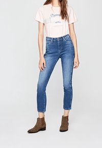 Ljusrosa t-shirt med kort ärm och grafisk design, kombinerad med blå högmidjade jeans. Accentuerad med bruna ankelstövlar i texturerat mocka.