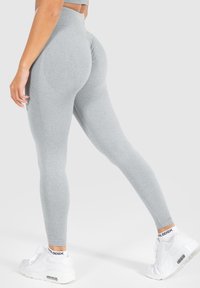 Grijze legging met een hoge tailleband, gestructureerd ontwerp, aansluitende pasvorm en een gladde stofafwerking, gecombineerd met witte sportschoenen.