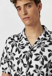 Kurzarmhemd in Weiß mit einem schwarzen Blumenmuster, ausgestattet mit einem Camp-Kragen und Knopfverschluss, aus leichtem Stoff gefertigt.