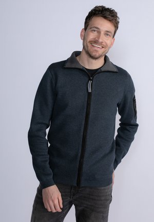 Navy zip-up sweater with a gray collar, made of soft fabric, featuring a black zipper and a pocket on the left arm.