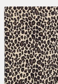 Le tissu à imprimé léopard présente un fond beige avec des taches de tailles variées en marron foncé et noir, créant une apparence texturée.