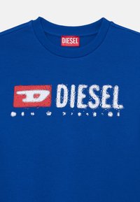 Modrá bavlnená tričko s okrúhlym výstrihom, na ktorom je textúrovaný červený a biely potlač "DIESEL". Tkanina vyzerá hladko a jednoducho.