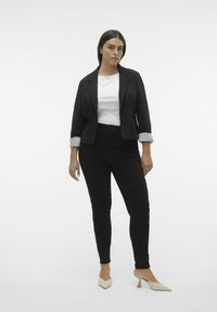 Sort blazer med rullede stribede manchetter over en hvid top, kombineret med sorte tætsiddende bukser og beige hælede mules. Neutral baggrund.