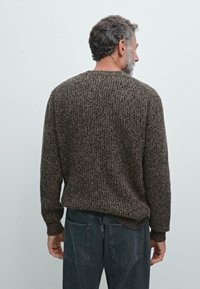 Brązowy sweter z dzianiny o teksturowanym wzorze, okrągłym dekolcie i długich rękawach, noszony z ciemnoszarymi dżinsami, widziany z tyłu.