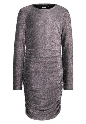 Dziewczyna w długim rękawie, marszczonej, srebrzystej metalicznej sukience, w połączeniu z białymi skarpetkami i białymi trampkami, stojąca z jedną nogą lekko wysuniętą do przodu.