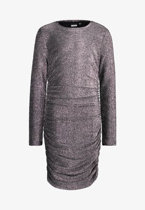 Pige iført en langærmet, rynket sølvmetallic kjole kombineret med hvide sokker og hvide sneakers, stående med det ene ben let fremme.