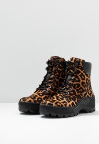 Kozáky s leopardím vzorem a černou gumovou podrážkou, texturovaná látka s potiskem zvířecí srsti, šněrování v přední části a polstrovaný límec pro pohodlí.