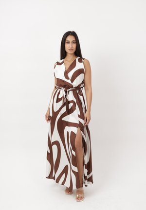 Mujer con un vestido largo sin mangas, estampado abstracto en marrón y blanco, con una abertura lateral y cintura anudada, de pie sobre un fondo blanco liso.