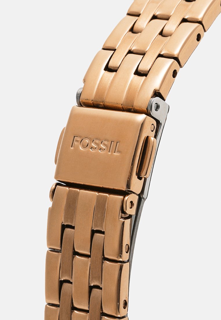 Roségoldene Metalluhr mit einem Verschluss, der mit "FOSSIL" graviert ist, verfügt über ein geflochtenes Linkdesign und einen Druckknopf-Entriegelungsmechanismus.