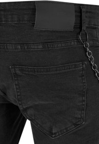 I jeans in denim nero presentano una tasca posteriore, una toppa in pelle e un accento di catena metallica attaccata in vita. Texture liscia con design classico.