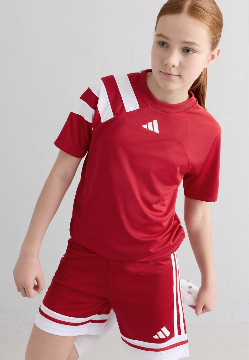 Rød idrettsskjorte med hvite striper, parret med røde shorts med hvite detaljer. Glatt, syntetisk stoff designet for bevegelse.