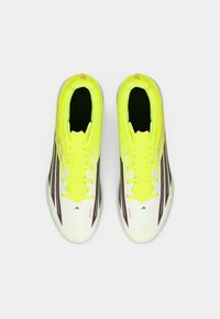 Φωτεινά κίτρινα ποδοσφαιρικά παπούτσια με λευκό επάνω μέρος, μαύρες ρίγες, μαύρη εσωτερική επένδυση και κίτρινες κορδόνες. Αθλητικός σχεδιασμός με υφή στην επιφάνεια.