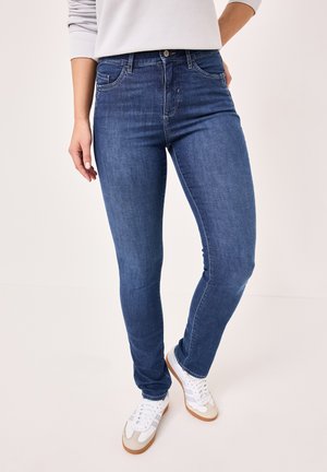 Skinny jeans in dark blue denim. Features front pockets, belt loops, and a slight fade along the leg. Paired with white and beige athletic shoes.