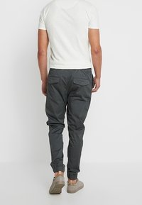 Szare joggery z elastycznymi ściągaczami i tylnymi kieszeniami, zestawione z dopasowanym białym T-shirtem. Buty to beżowe sneakersy.