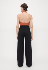 Brown halter top with pleated neckline paired with high-waisted, wide-leg black trousers, visible seam detailing along the waist.