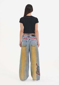 Black cropped t-shirt and wide-leg denim jeans. Jeans feature an ombre effect from blue to yellow, with embroidered accents on the leg and back.
