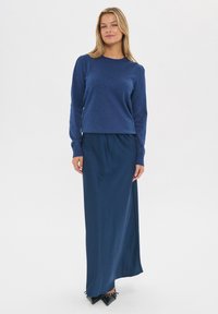 Marineblauwe gebreide trui met lange mouwen, gecombineerd met een lange, flowy marineblauwe rok. Beide stukken hebben een zachte textuur en een relaxte pasvorm.