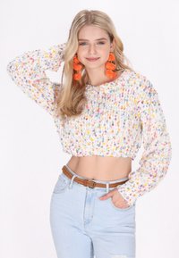 Maglione corto multicolore con texture a maglia grossa e maniche lunghe, caratterizzato da una base bianca e macchie colorate; abbinato a jeans chiari.