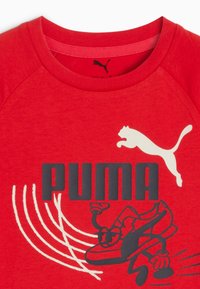 Röd bomulls t-shirt med en svart "PUMA"-logotyp och en grafik av en löpsko. Accentuerad med vita linjer och en vit hoppande puma.