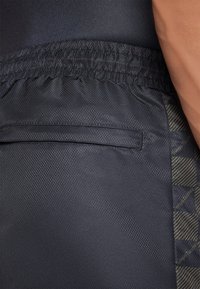 Pantalones cortos deportivos negros con una tela texturizada que presenta un sutil patrón geométrico y una cintura elástica. Incluye un detalle de bolsillo lateral.