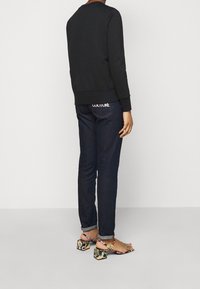 Svart sweatshirt med ribbade muddar, matchad med mörkblå jeans som har en logotyp på bakfickan och blommönstrade klacksandaler.