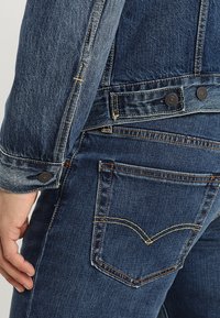 Jeansjacka med en mörkblå tvätt, klassisk passform, öppen krage, knappade manschetter med metalldetaljer och distinkta sömnadsdetaljer.