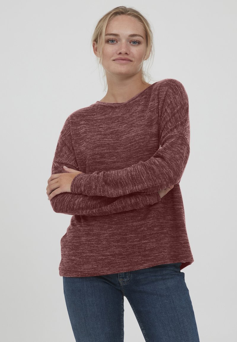 Burgunderfarget langermet genser med en avslappet passform, teksturert stoff, ribbet mansjetter og rund hals. Kombinert med blå jeans.