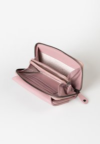 Roze leren portemonnee met een ritssluiting. Het interieur heeft meerdere kaartsleuven, compartimenten en een subtiele patroonvoering. Fluweelachtige textuur.