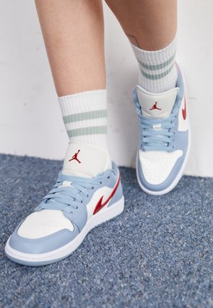 Baskets bleu clair avec un capuchon blanc et des accents rouges, présentant une texture lisse, des lacets plats, et un logo sur la languette et le côté.