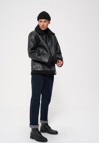 Czarna skórzana kurtka bomberka z kołnierzem z owczej wełny, zestawiona z ciemnym dżinsami podwiniętymi na mankietach i czarnymi sznurowanymi botkami.