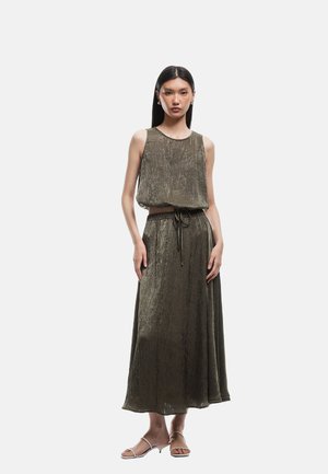 Olijfgroene mouwloze jurk met een gestructureerde afwerking, een getailleerde taille en een vloeiende rok. Gecombineerd met minimalistische sandalen.
