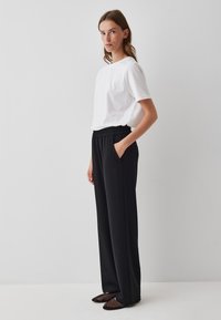 Zwarte, wijde broek met een elastische tailleband en zijzakken, gecombineerd met een eenvoudig wit t-shirt met korte mouwen en zwarte mesh schoenen.