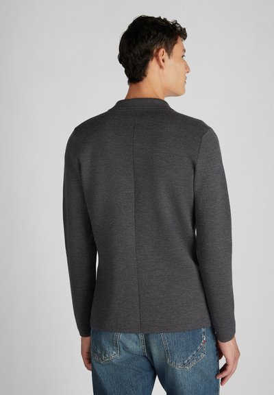Graues Langarmoberteil mit hohem Kragen, das eine gerade Naht auf der Rückseite aufweist. Kombiniert mit blauen Jeans. Weiche Textur.
