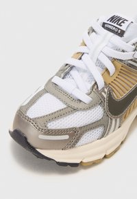 Nike Vomero 5 tenisice imaju gornji dio od bijele mreže s srebrnim i zlatnim akcentima, zatvaranje na pertlanje te teksturirani gumeni potplat.